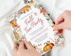 A person's hands holding a printed fall tea party invitation card over white fabric. The card features autumn watercolor illustrations including orange pumpkins, fall leaves, flowers, and a teapot, with the text 'Fall Tea Party' in large red script.