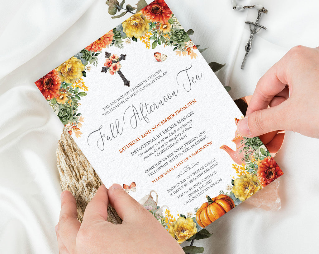 A floral fall afternoon tea invitation card is being held by two hands over white satin fabric, with a small cross and wrapped gift box nearby.