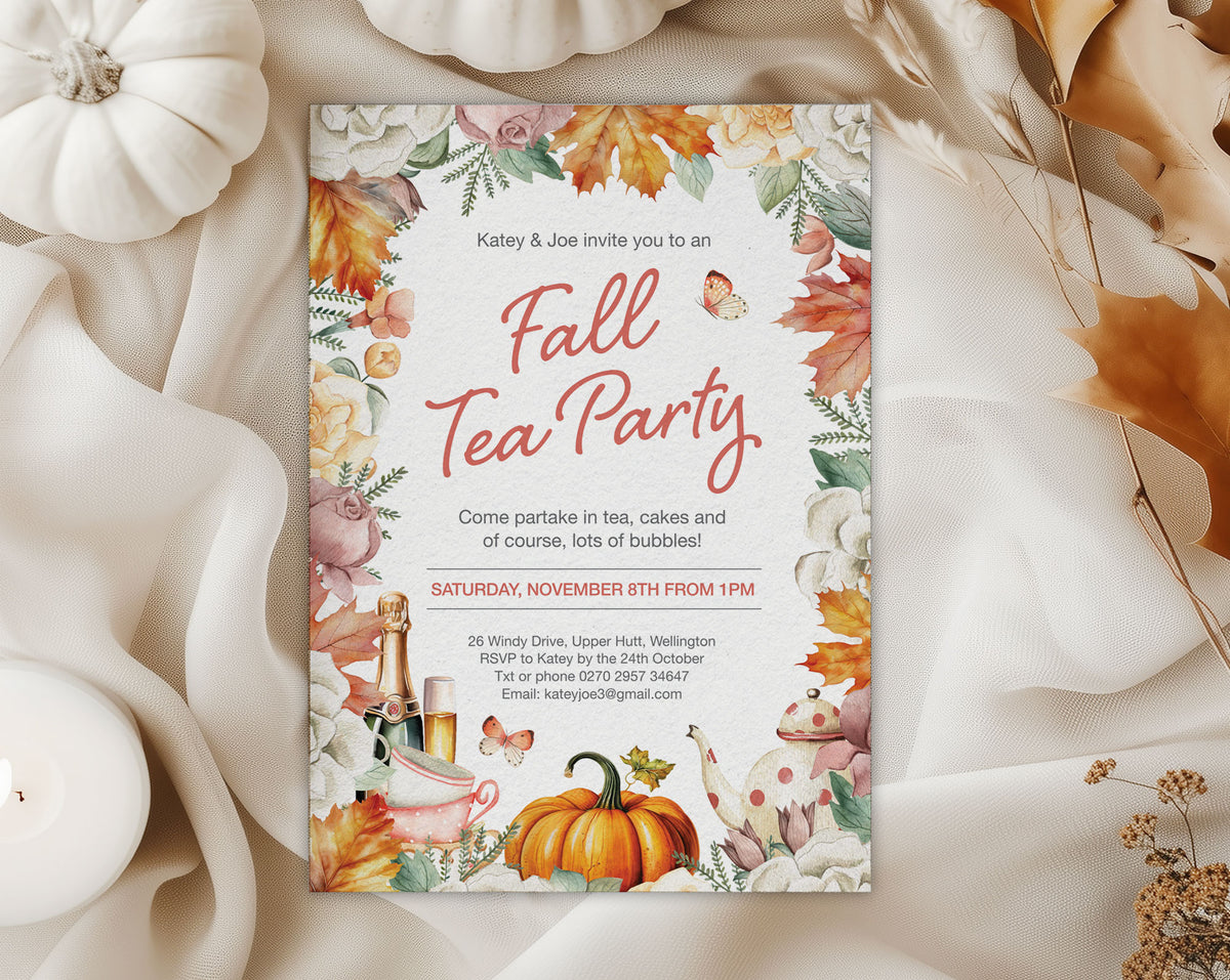 A fall-themed tea party invitation card styled in a flat-lay arrangement with white fabric, dried leaves, and small pumpkins. The card features a watercolor floral border with orange, pink, and yellow autumn leaves, a teapot, and the text 'Fall Tea Party' in coral script.