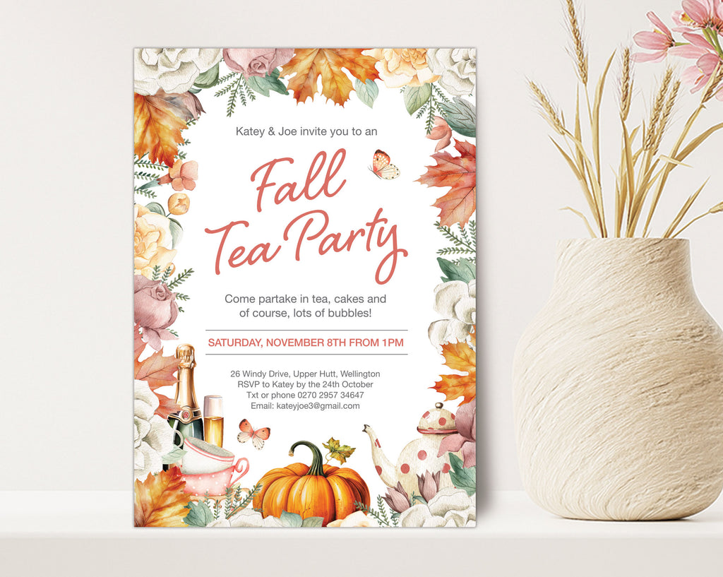 A vertical fall-themed tea party invitation card displayed on a white surface next to a textured cream vase with dried wheat stems. The invitation features a watercolor autumn border with orange pumpkins, fall leaves, teapots, and butterflies, with the text 'Fall Tea Party' in coral script.