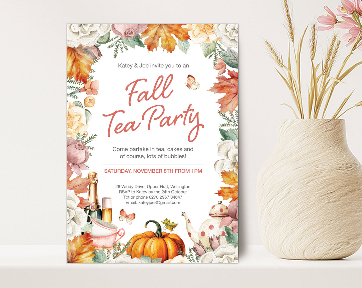 A vertical fall-themed tea party invitation card displayed on a white surface next to a textured cream vase with dried wheat stems. The invitation features a watercolor autumn border with orange pumpkins, fall leaves, teapots, and butterflies, with the text 'Fall Tea Party' in coral script.