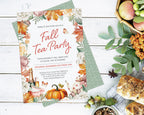 A styled flat-lay of an autumn-themed tea party invitation card on top of a green patterned paper, surrounded by fall props including apples, bread, nuts, and leaves on a white wood background.