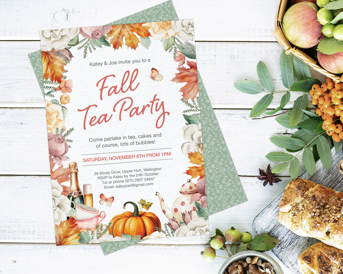 A styled flat-lay of an autumn-themed tea party invitation card on top of a green patterned paper, surrounded by fall props including apples, bread, nuts, and leaves on a white wood background.