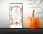 A smartphone mockup displays a fall-themed tea party invitation with floral autumn illustrations and orange script text. A real orange pumpkin sits beside the phone on a dark surface against a light gray background with soft shadows.