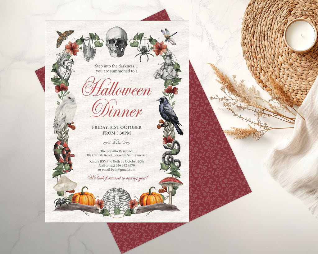 A Halloween dinner invitation card with illustrated seasonal motifs like a skull, owl, spider, raven, pumpkin, and mushrooms, placed on top of another invite showing the patterned burgundy back on a light marble surface with a woven placemat and candle nearby.