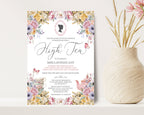 High tea invitation with floral design on a white surface next to a vase with flowers.