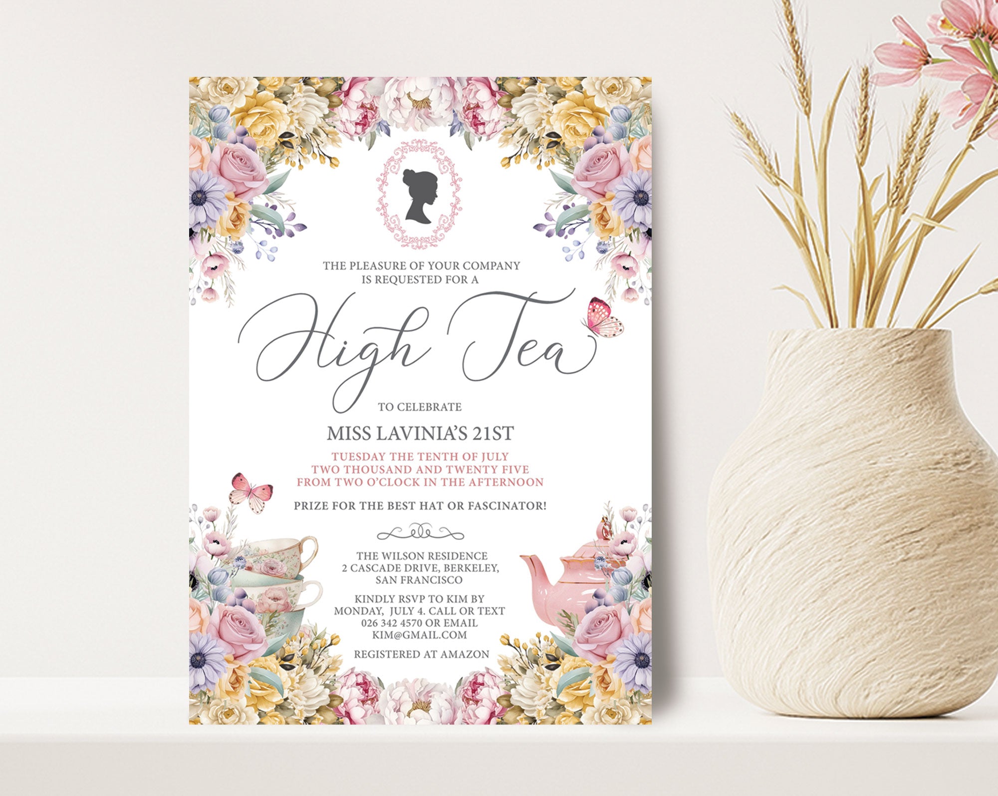 High tea invitation with floral design on a white surface next to a vase with flowers.