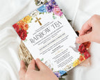 two hands holding a rainbow tea church event invitation with bright flowers, gold cross and teapot, with a white silk cloth in the background