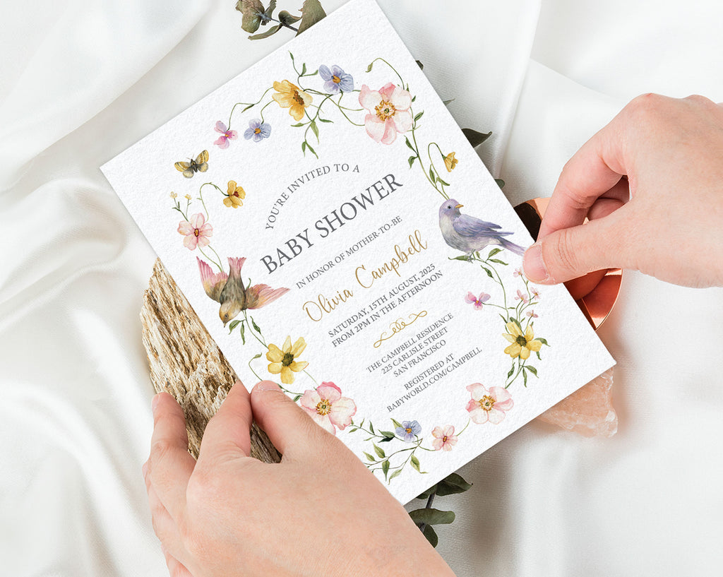 Baby shower invitation with floral and bird design held by hands on a light background