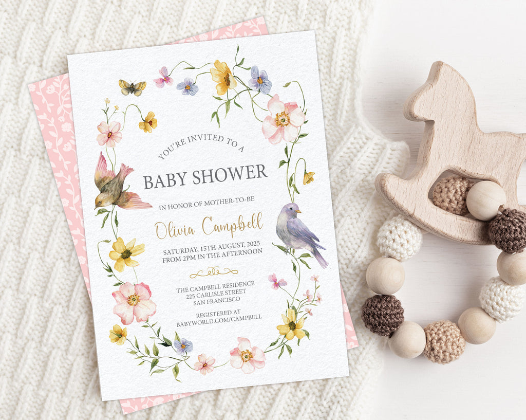 Baby shower invitation with flowers and birds on a cream knited blanket with a teething toy.