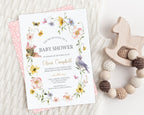 Baby shower invitation with flowers and birds on a cream knited blanket with a teething toy.