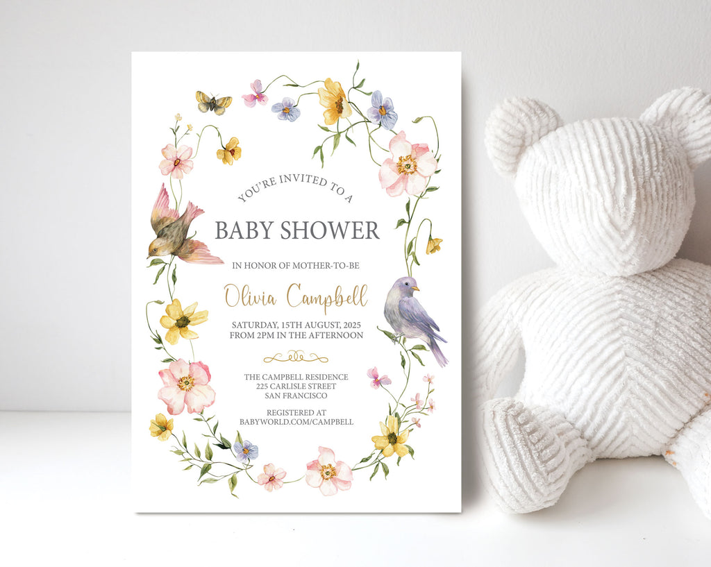 pretty blue yellow and pink Baby shower invitation with floral design and birds leaning up against a white wall next to a white teddy bear