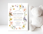 pretty blue yellow and pink Baby shower invitation with floral design and birds leaning up against a white wall next to a white teddy bear