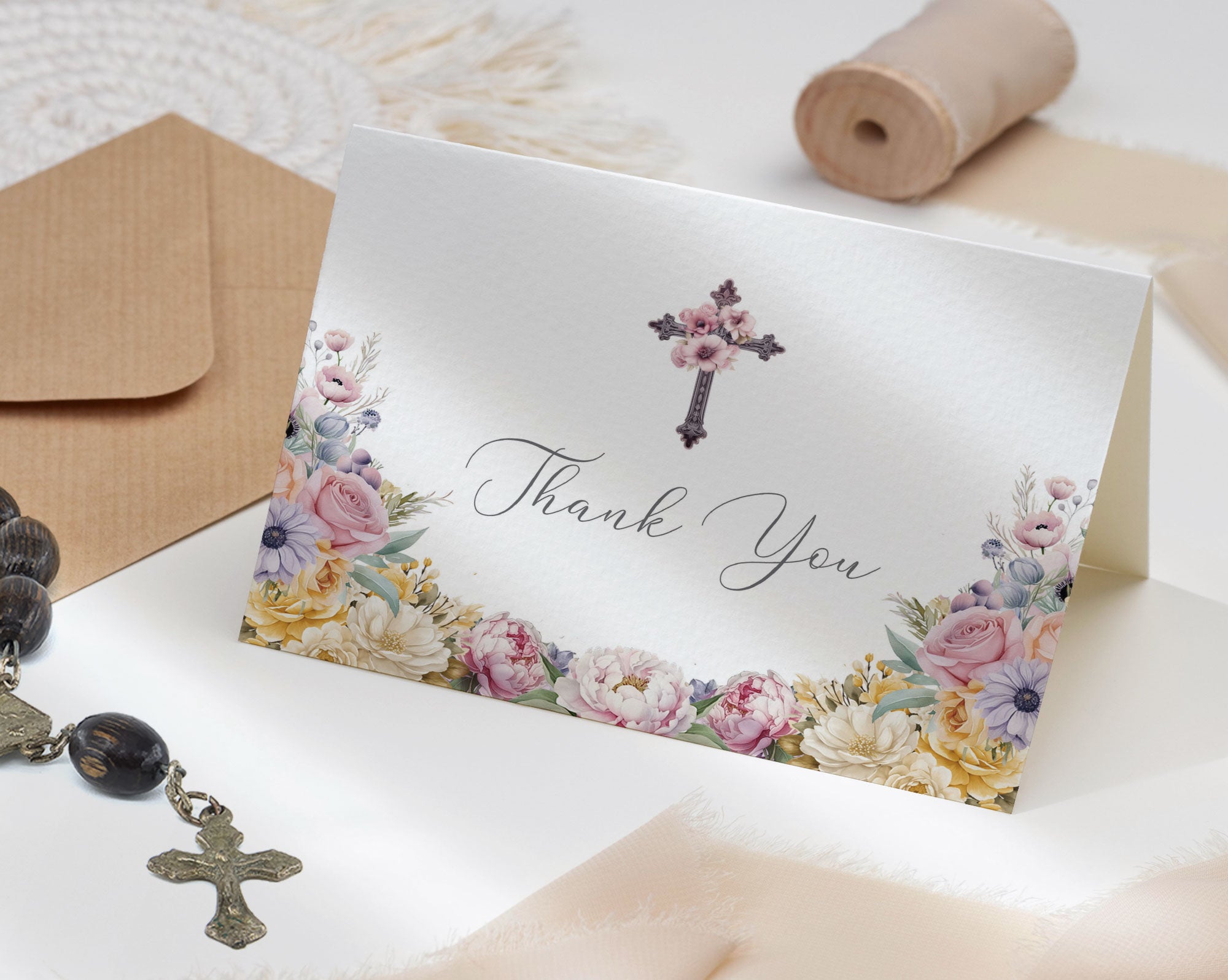 church thank you tent card with floral design and cross, placed on a textured surface with ribbon roll, envelope and rosary.