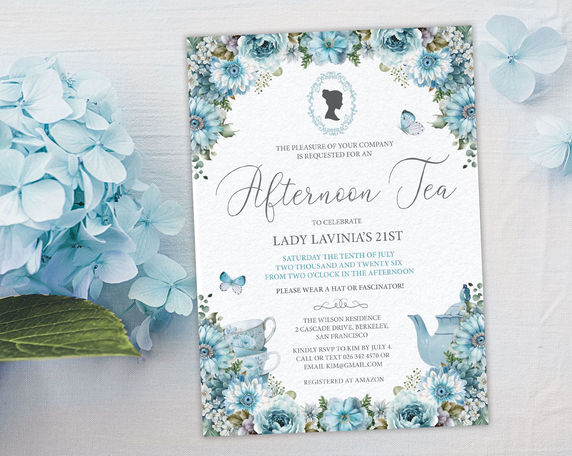 elegant dusty blue flower Invitation card for an afternoon tea celebration on a white surface next to blue hydrangea