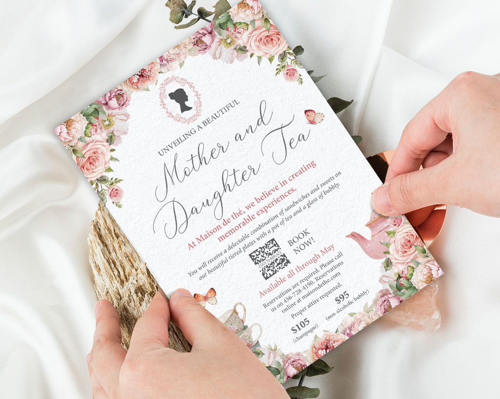 two hands holding a mother and daughter tea business event invitation with cameo and teapot graphics over a white background