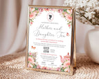 a gold frame with a mother and daughter tea invitation with cameo and QR code showing on a rattan mat next to a vase of white flowers