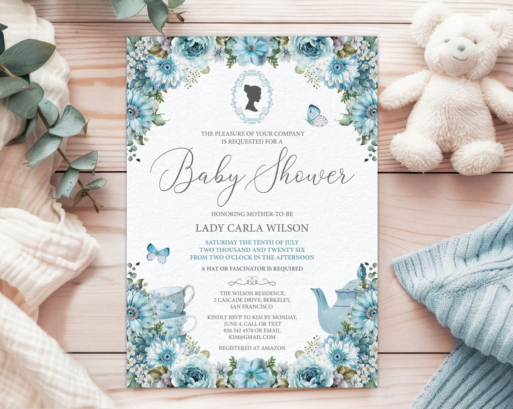 an elegant blue baby shower tea regency style invitation laying on the pink pattern back of the invite, on a white cloth with a white teddy bear and a wrapped gift