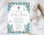a dusty blue flower baby shower tea invitation with cameo and teapot, laying on a wooden background next to a white teddy bear, some baby blankets and eucalyptus