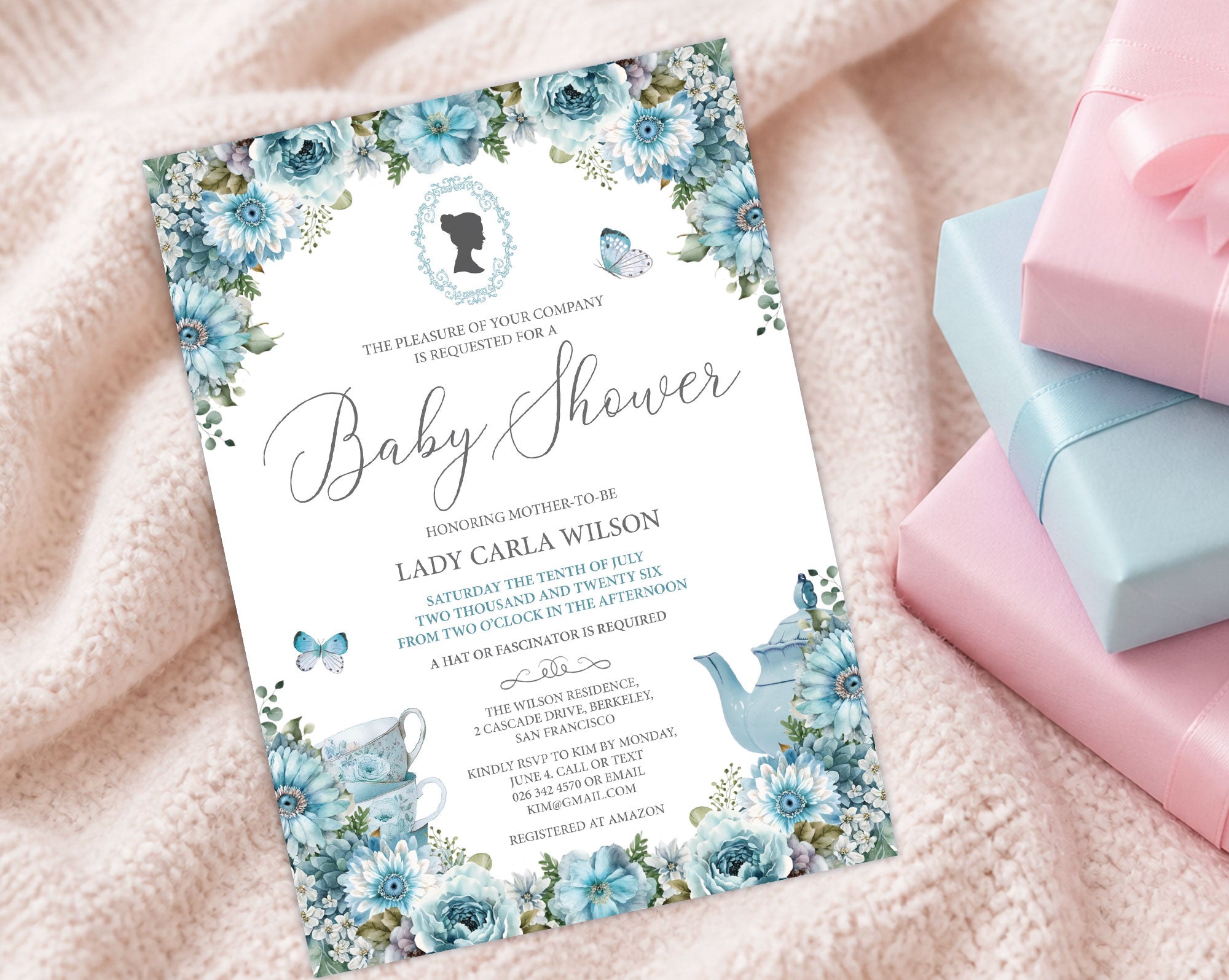 a dusty blue baby shower invitation with cameo and flowers on a cream baby blanket next to some pink and blue wrapped gifts