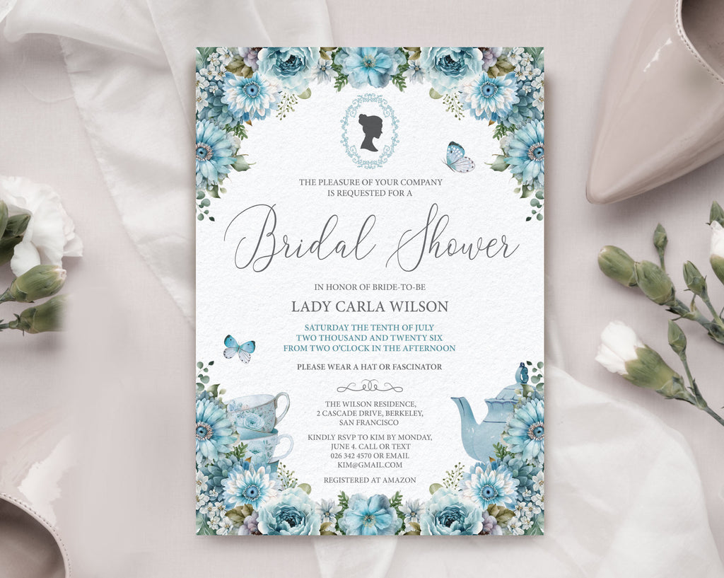 Pretty dusty blue flower bridal shower invitation laying on a beige silk background with a wedding shoe and some flowers