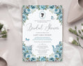Pretty dusty blue flower bridal shower invitation laying on a beige silk background with a wedding shoe and some flowers