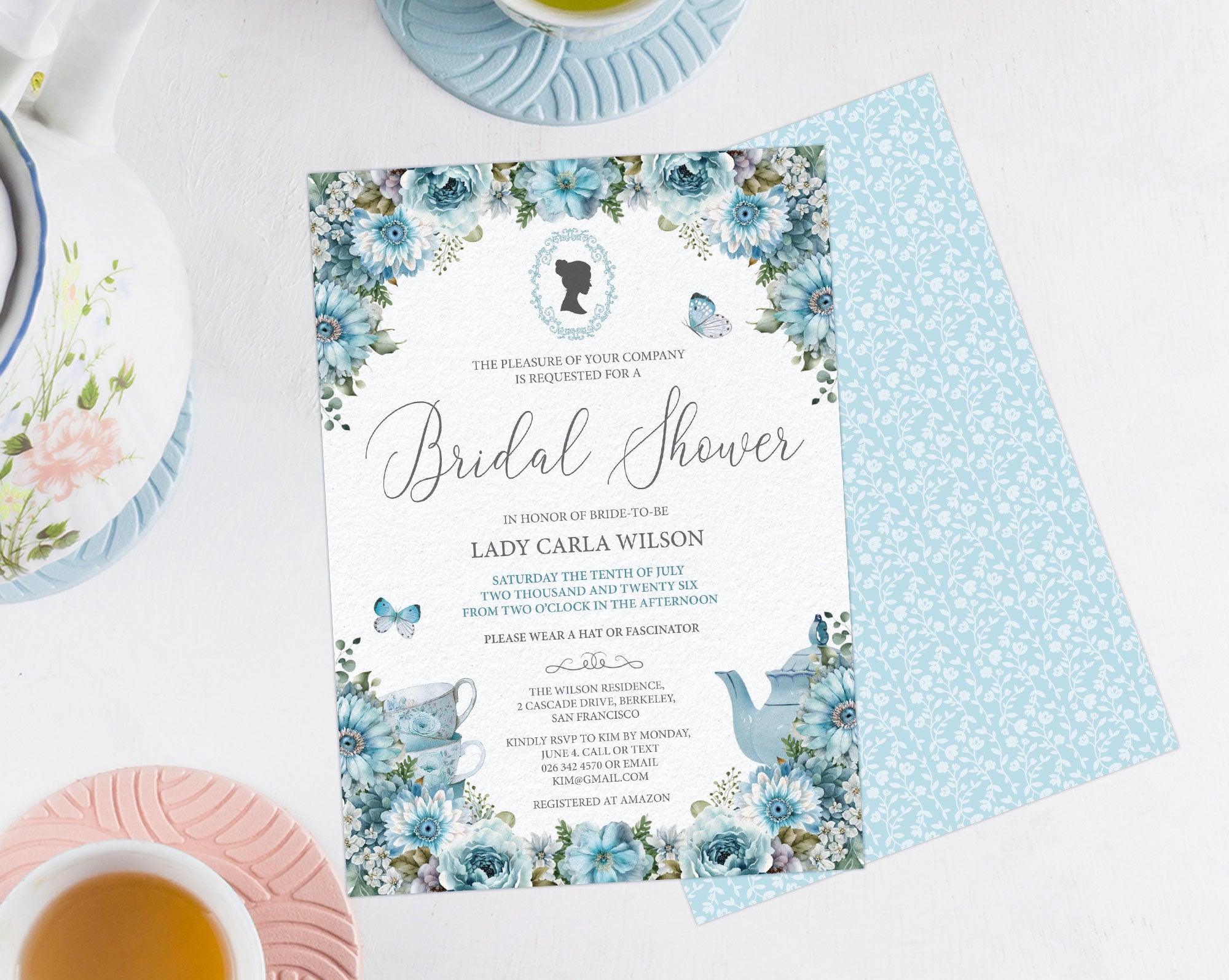elegant blue flower bridal shower invitation showing the front and the back with the blue pattern background, laying on a grey background with a pretty pastel tea servies