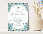 a 5 x 7 blue flower bridal shower invitation with victorian cameo, leaning up against a beige wall next to a vase full of dried blue flowers