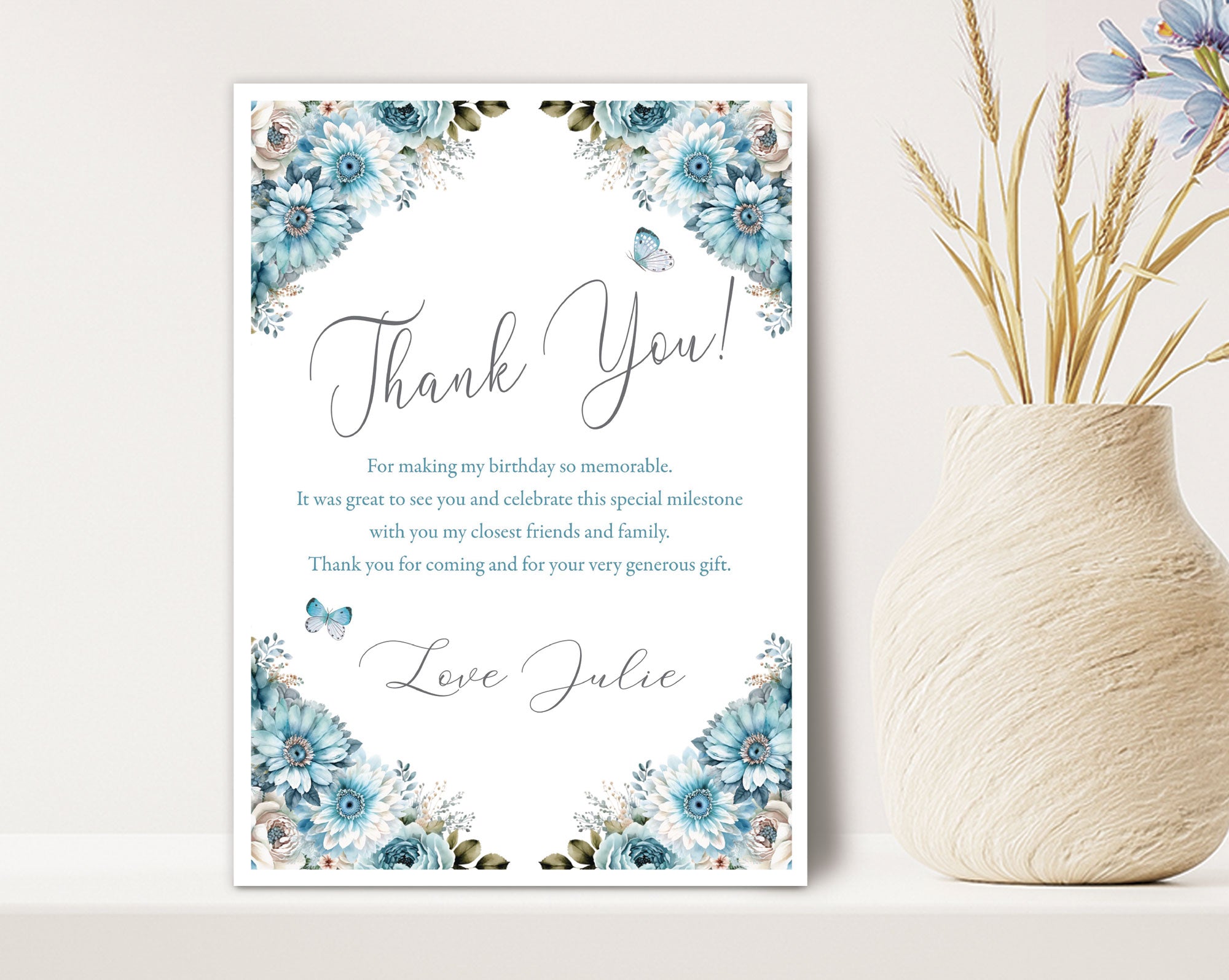 dusty blue thank you note with butterfly graphics leaning against a white wall next to a vase full of dried flowers