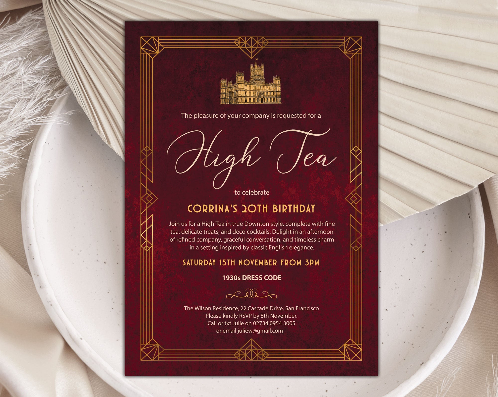 an elegant red velvet and gold art deco styled downton high tea invitation laying on a plate with a dried leaf