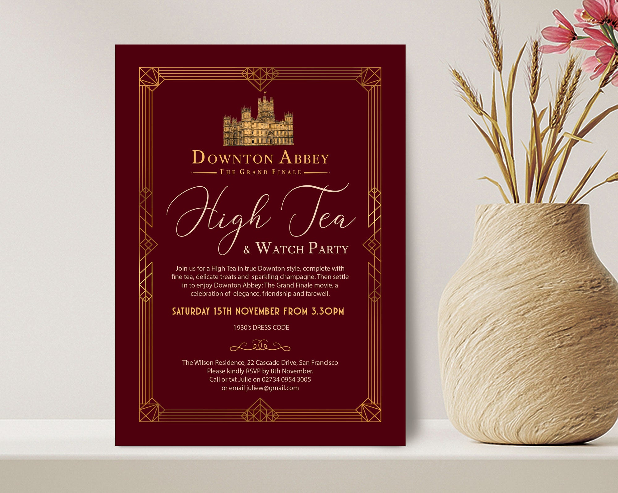 elegant burgundy velvet and gold art deco styled birthday invitation leaning up against a wall on a shelf next to a vase of dried flowers