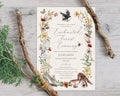 an enchanted forest evening invitation on recycled card laying on a grey wooden background with two tree twigs and greenery