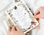 two hands holding a pretty enchanted forest evening dinner invitation with white cloth in the background