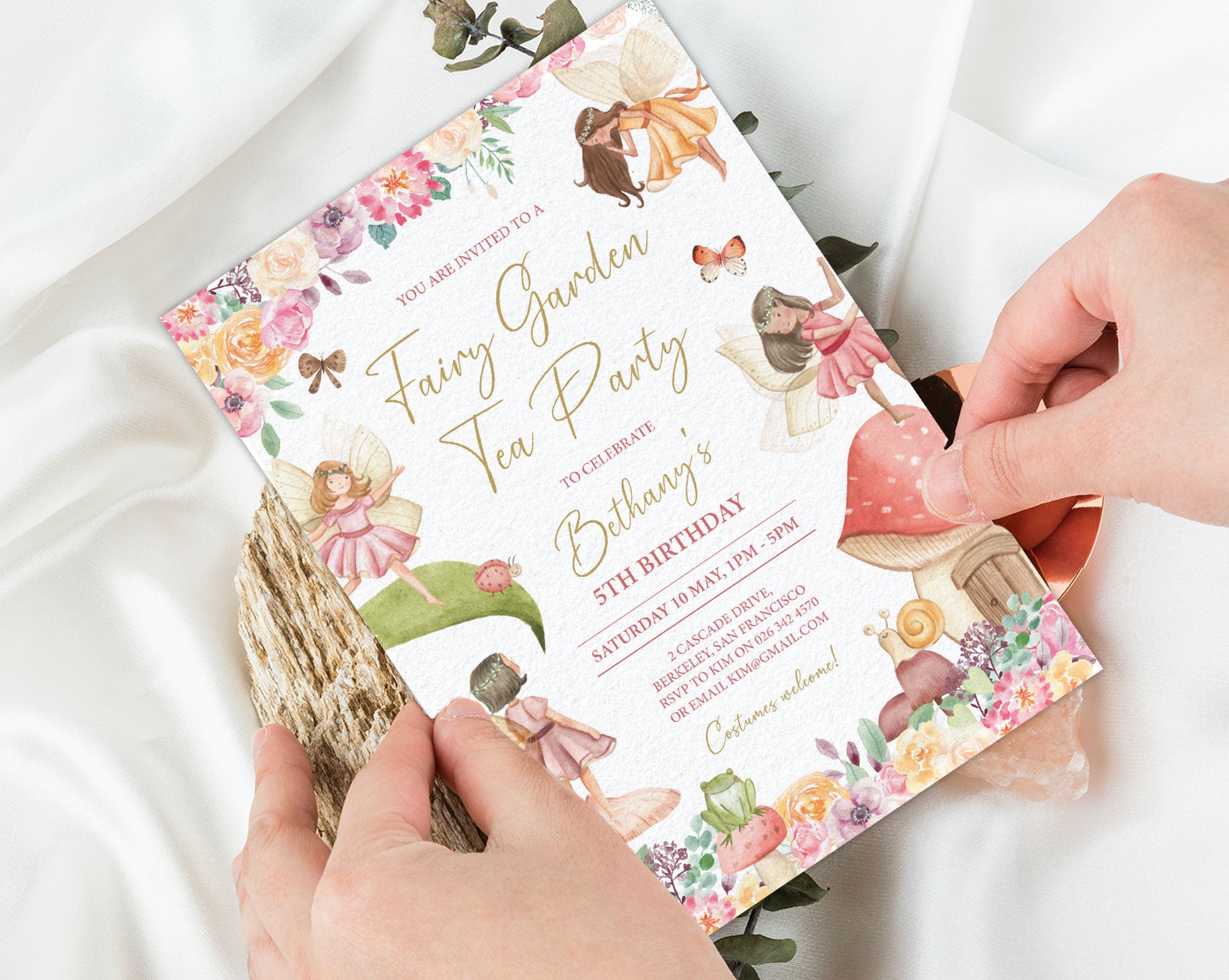 two hands holding a fairy garden tea party invitation with a white silk background
