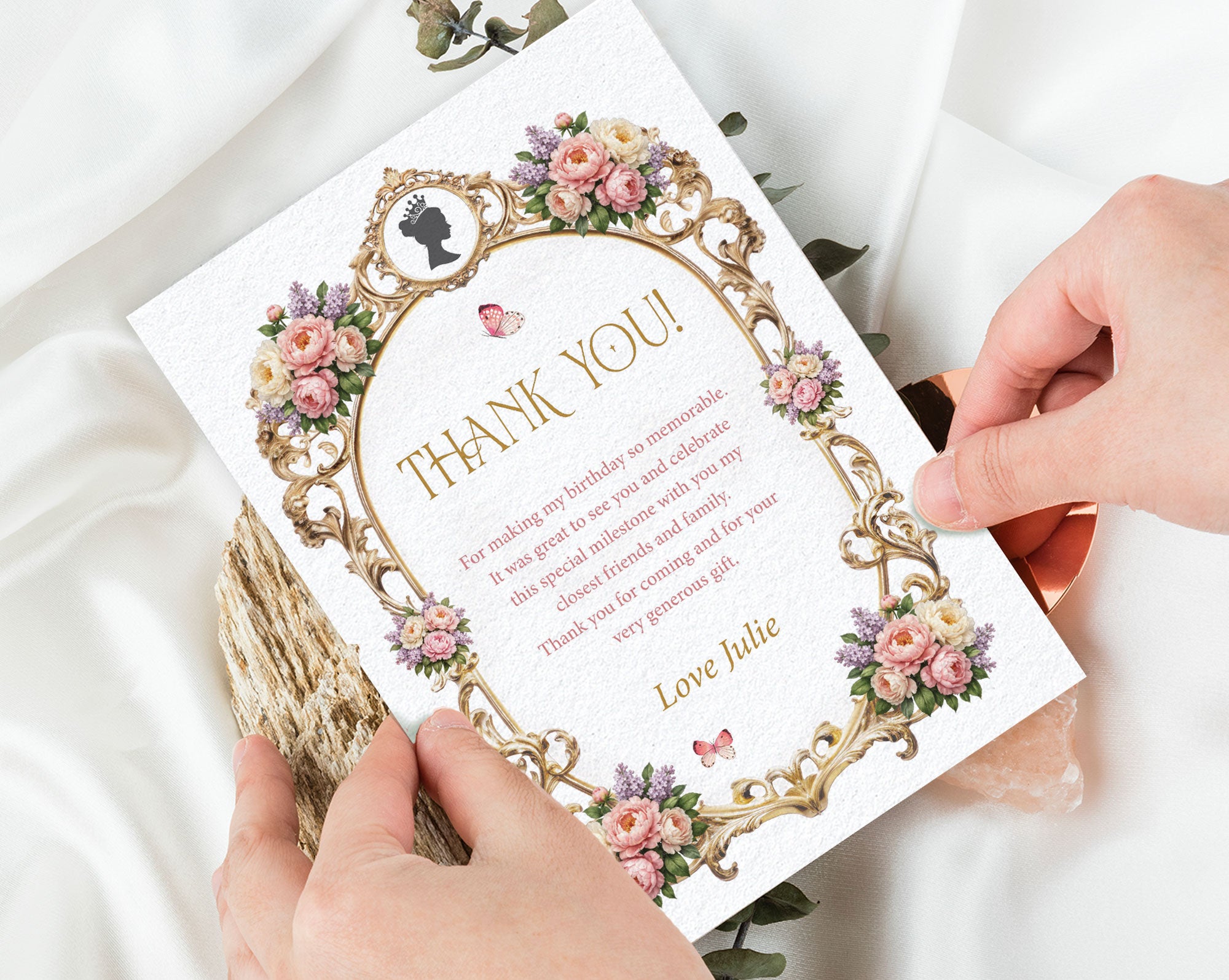 2 hands holding an elegant royal thank you note, with peonies, gold frame and cameo graphics with white silk in the background