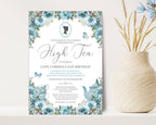 pretty blue flower Invitation card for an high tea event with bridgerton-inspired cameo on a white surface next to a vase of dried flowers.