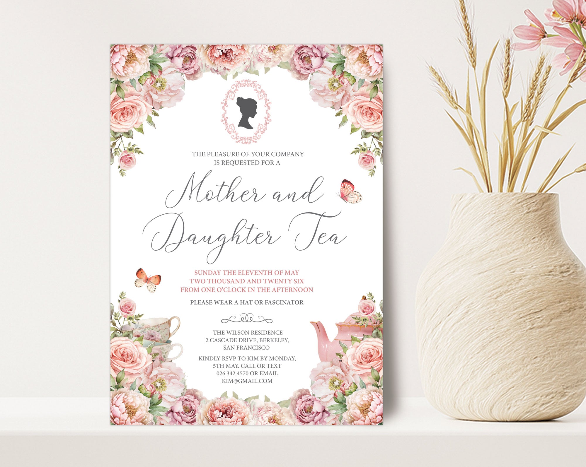 a 5 x 7 mother and daughter tea invitation standing up against a beige wall next to a vase of dried flowers
