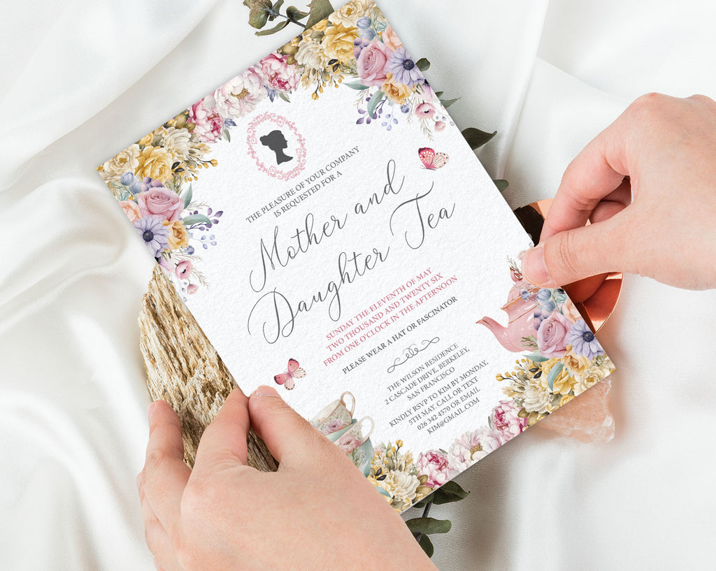 to hands folding a pastel Floral invitation card for a Mother and Daughter Tea event on a white fabric background.