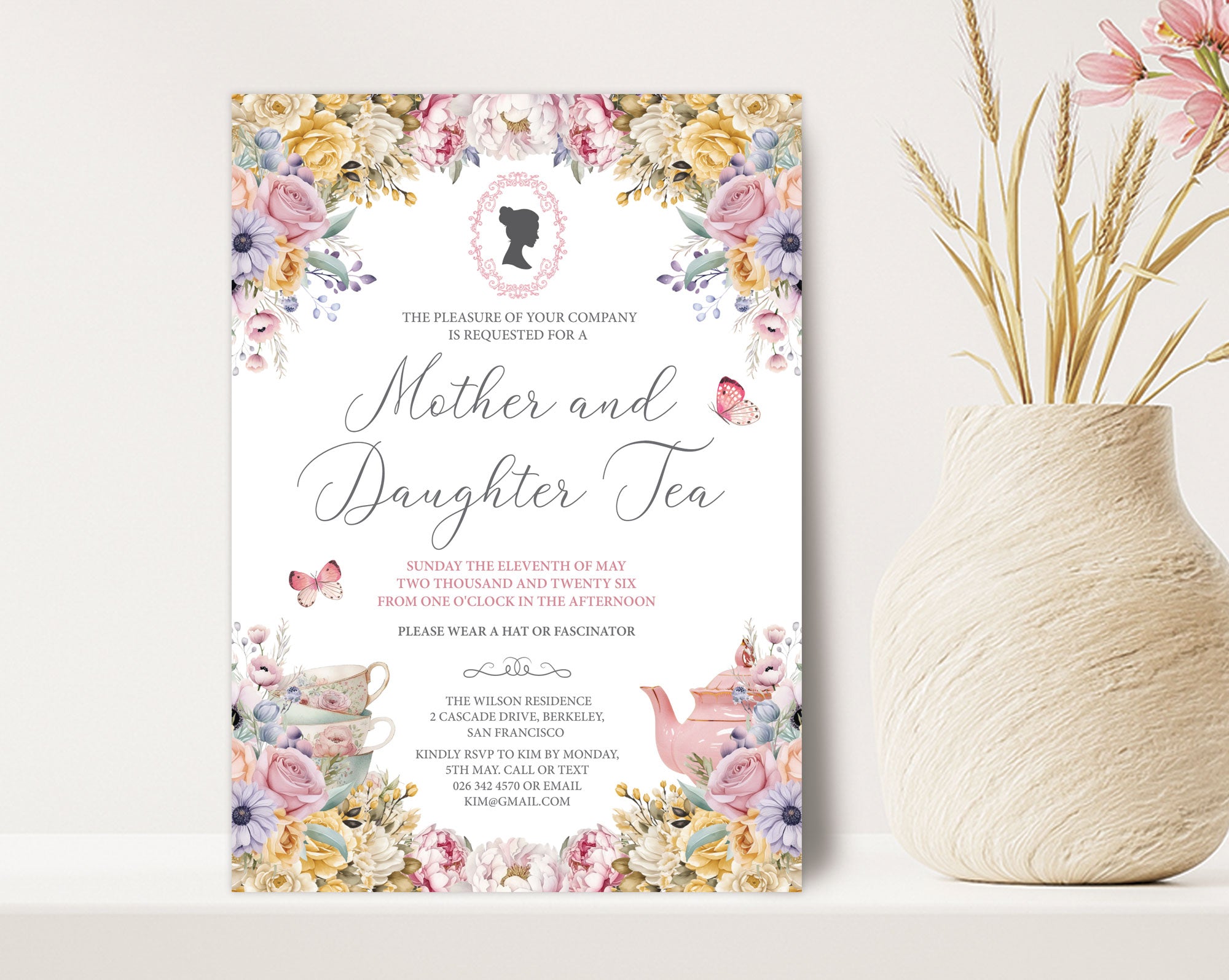 a 5 x 7 mother and daughter tea invitation standing up against a beige wall next to a vase of dried flowers