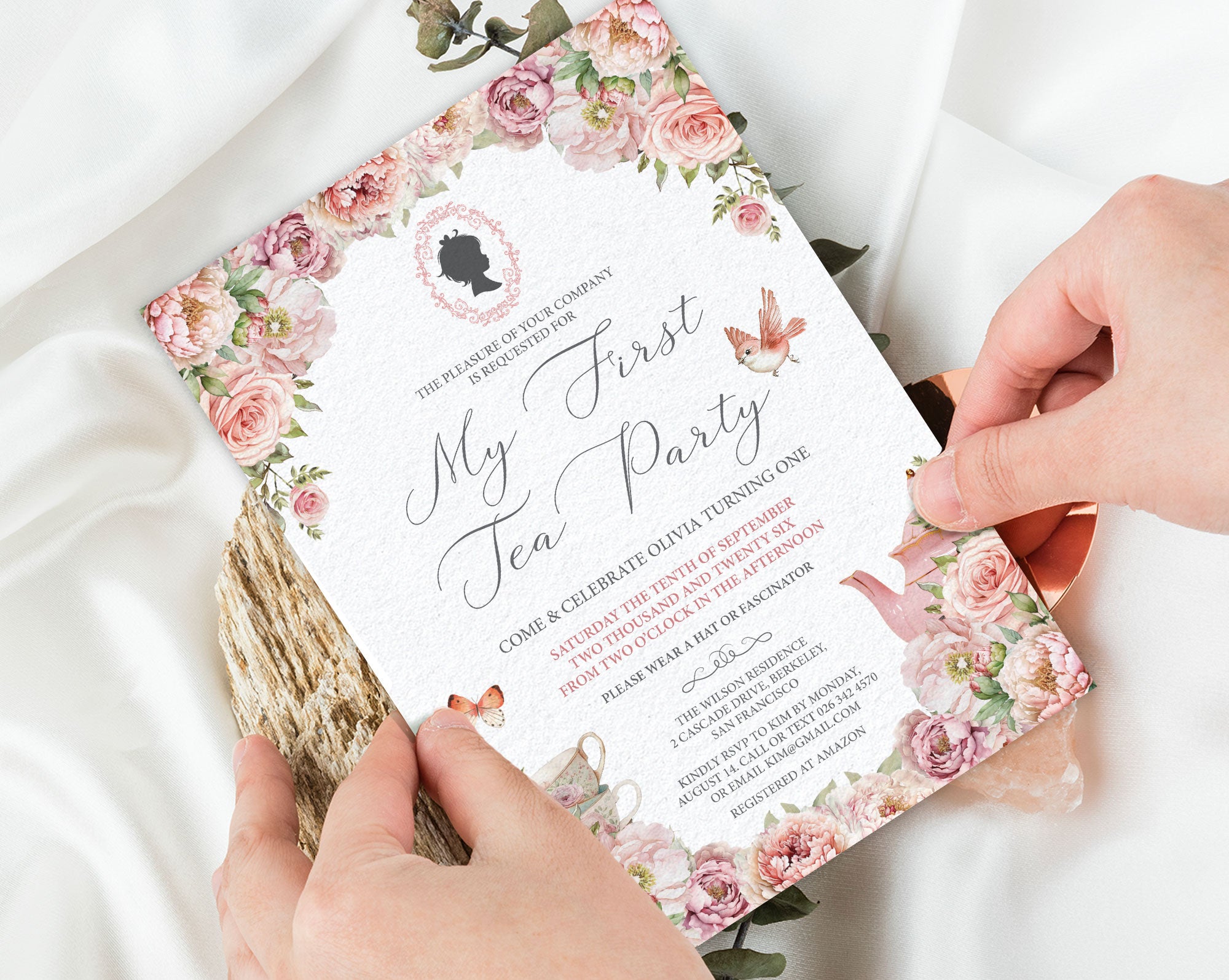 Bridgerton Inspired Invitation card for a 'My First Tea Party' with floral design held by hands on a white fabric background.
