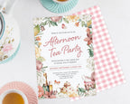afternoon tea party invitation with floral border, showing the pink gingham back, laying on a white background next to a pastel tea set