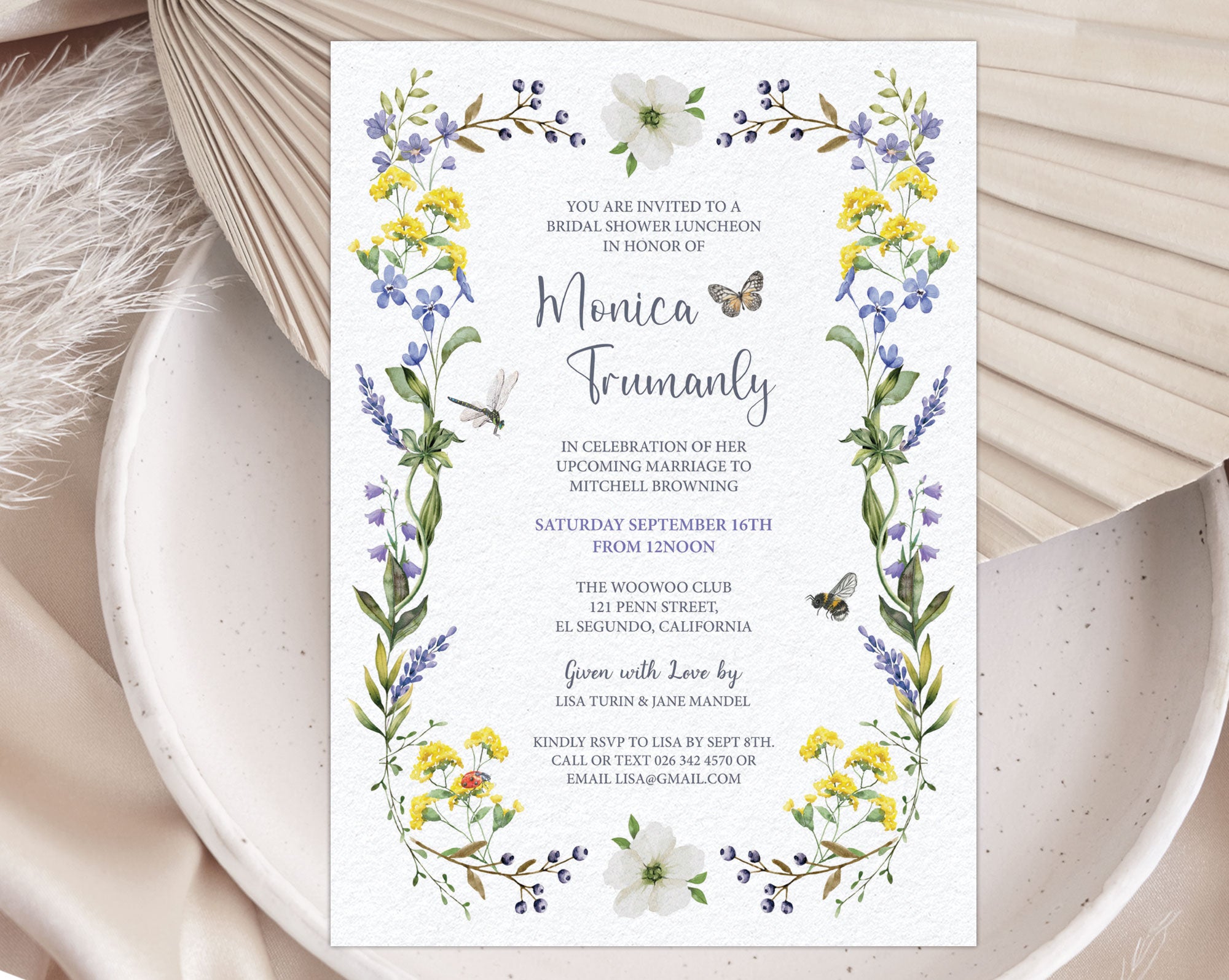 A bridal shower luncheon invitation with wildflowers and butterfly laying on a white plate with a dried leaf in the background