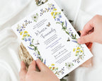 2 hands holding a bridal shower lunch invitation with purple and yellow wildflower border, ladybug, bee, dragonfly and butterfly graphics