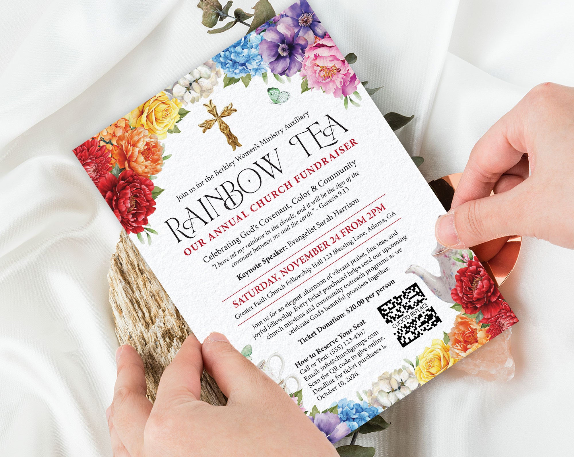 two hands holding a rainbow tea church rainbow money raising event invitation with bright flowers, gold cross and teapot, with a white silk cloth in the background