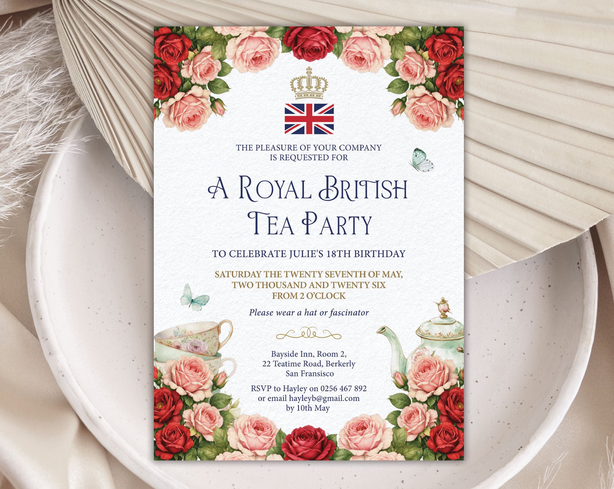 Invitation card for a Royal British Tea Party with red and pink roses, teapot, crown and flag logo and butterflies on a white plate with a dried leaf