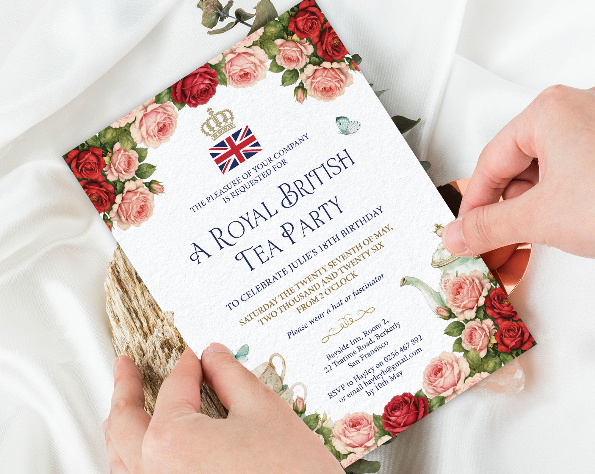 Invitation card for a Royal British Tea Party held by hands on a white fabric background