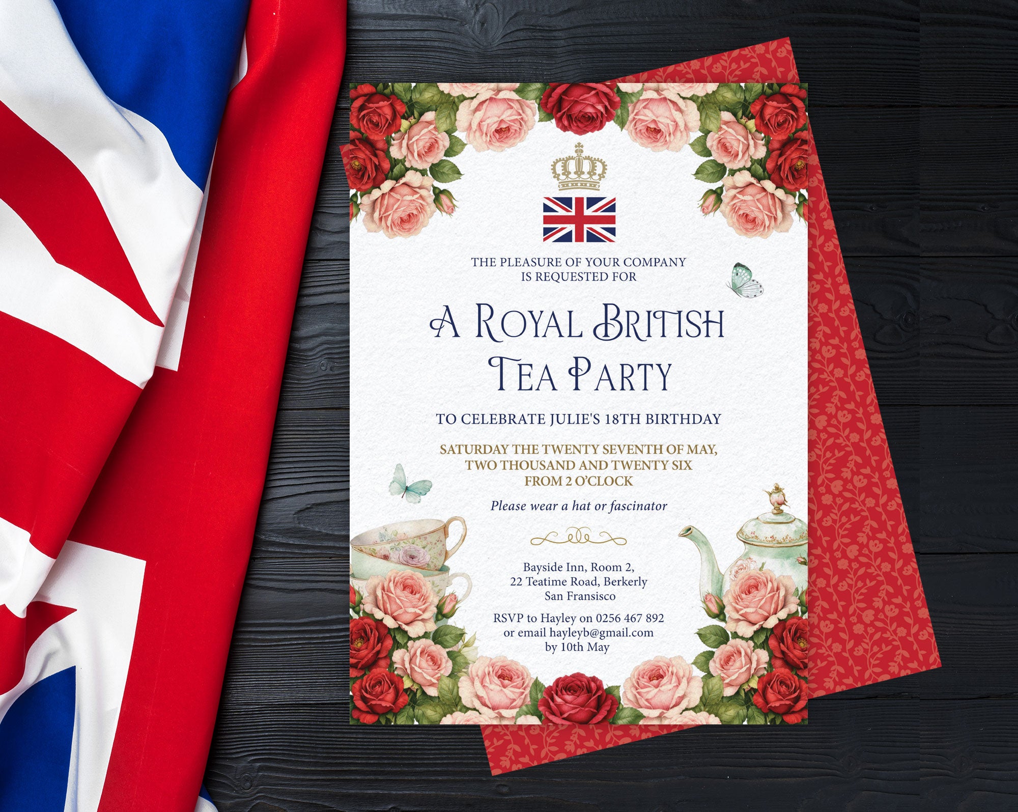 Invitation card for a Royal British Tea Party with red and pink rose design and Union Jack flag on a black wooden surface.