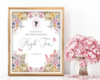 Pretty pastel high tea sign in a gold frame with floral design, cameo next to pink flowers in a vase.