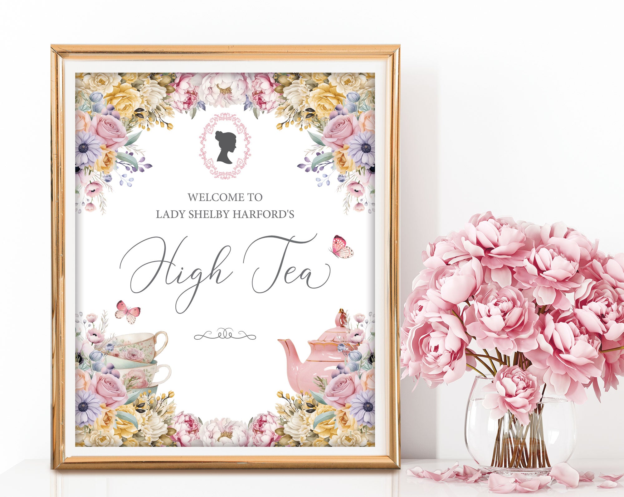Pretty pastel high tea sign in a gold frame with floral design, cameo next to pink flowers in a vase.