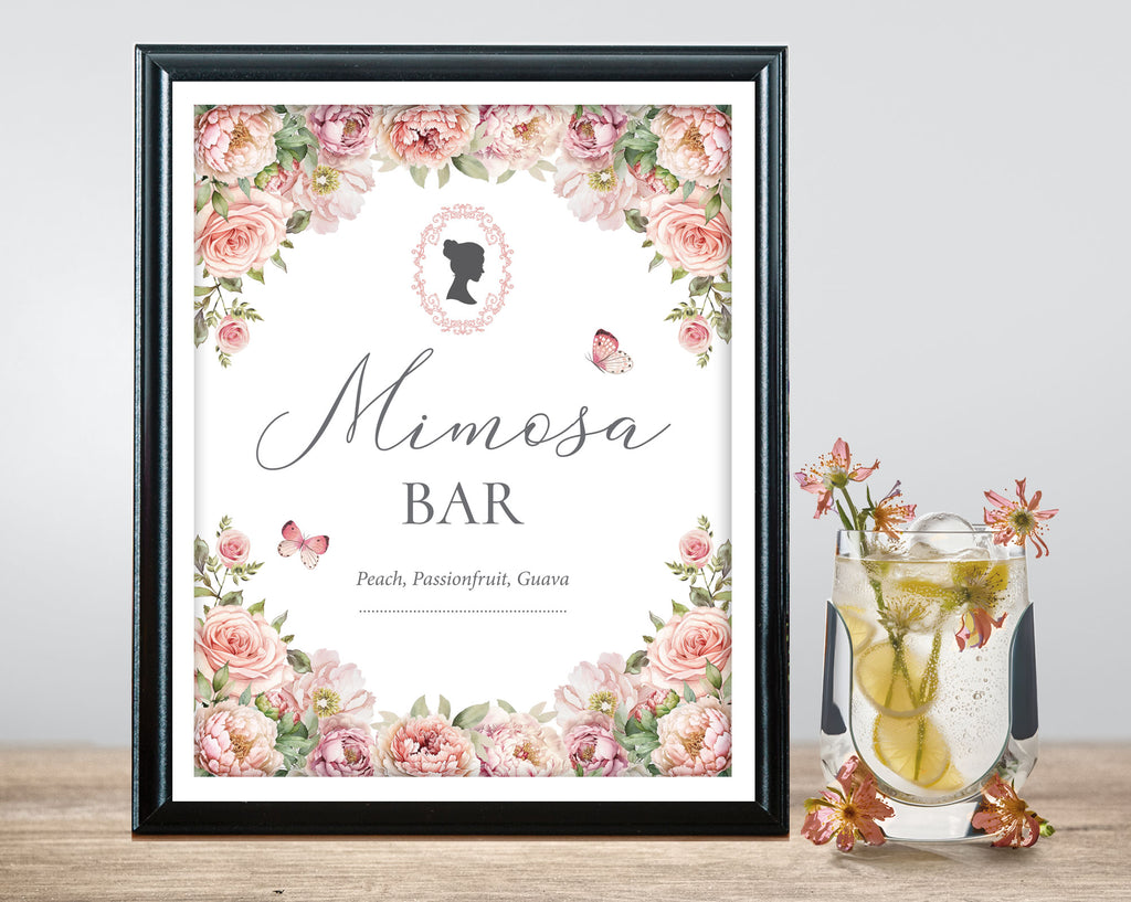 Framed 'Mimosa Bar' sign with blush pink floral design next a glass of mimosa on a wooden surface.
